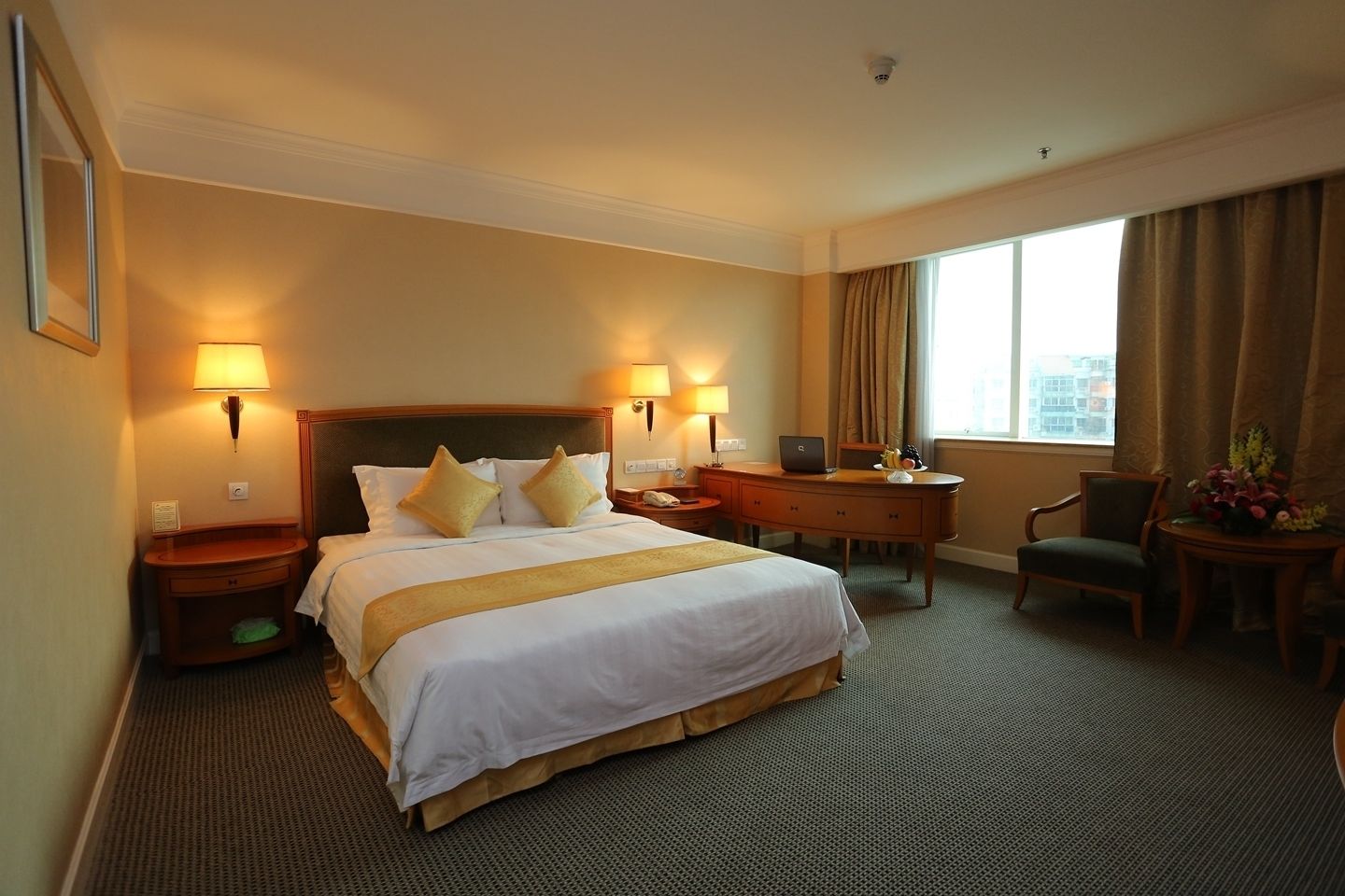 Une chambre d’hôtel avec un grand lit, deux tables de chevet avec des lampes, un bureau, une chaise et une vue sur la ville par la fenêtre.