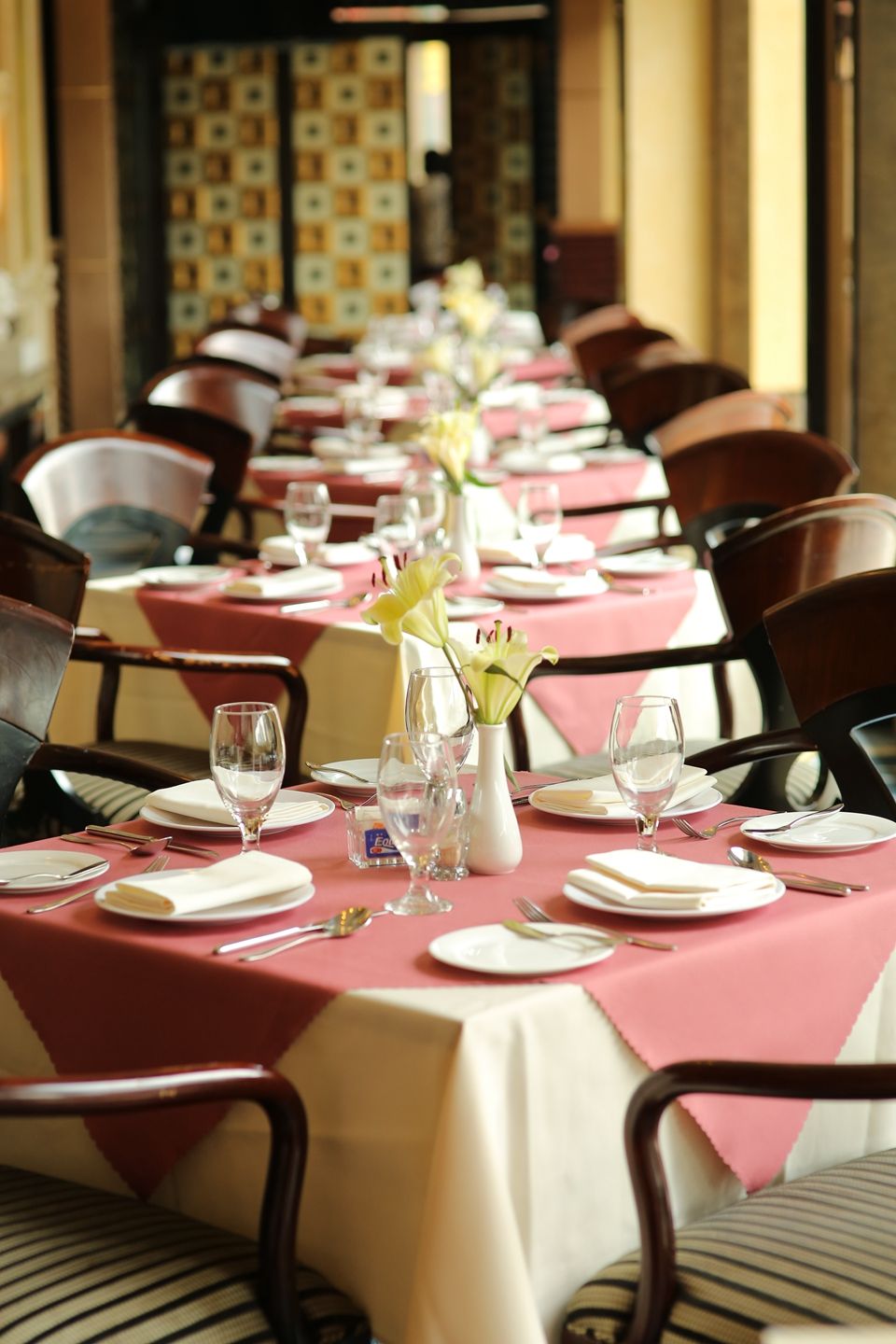 A long dining table with pink tablecloths, white plates, and clear glassware.