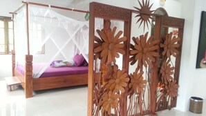 A room with a wooden four-poster bed, a decorative wooden partition with floral designs, and a white floor. - Hotel Orangutan (Bukit Lawang)