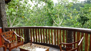 A wooden deck with a table and chairs, surrounded by a stone wall and lush greenery. - Hotel Orangutan (Bukit Lawang)