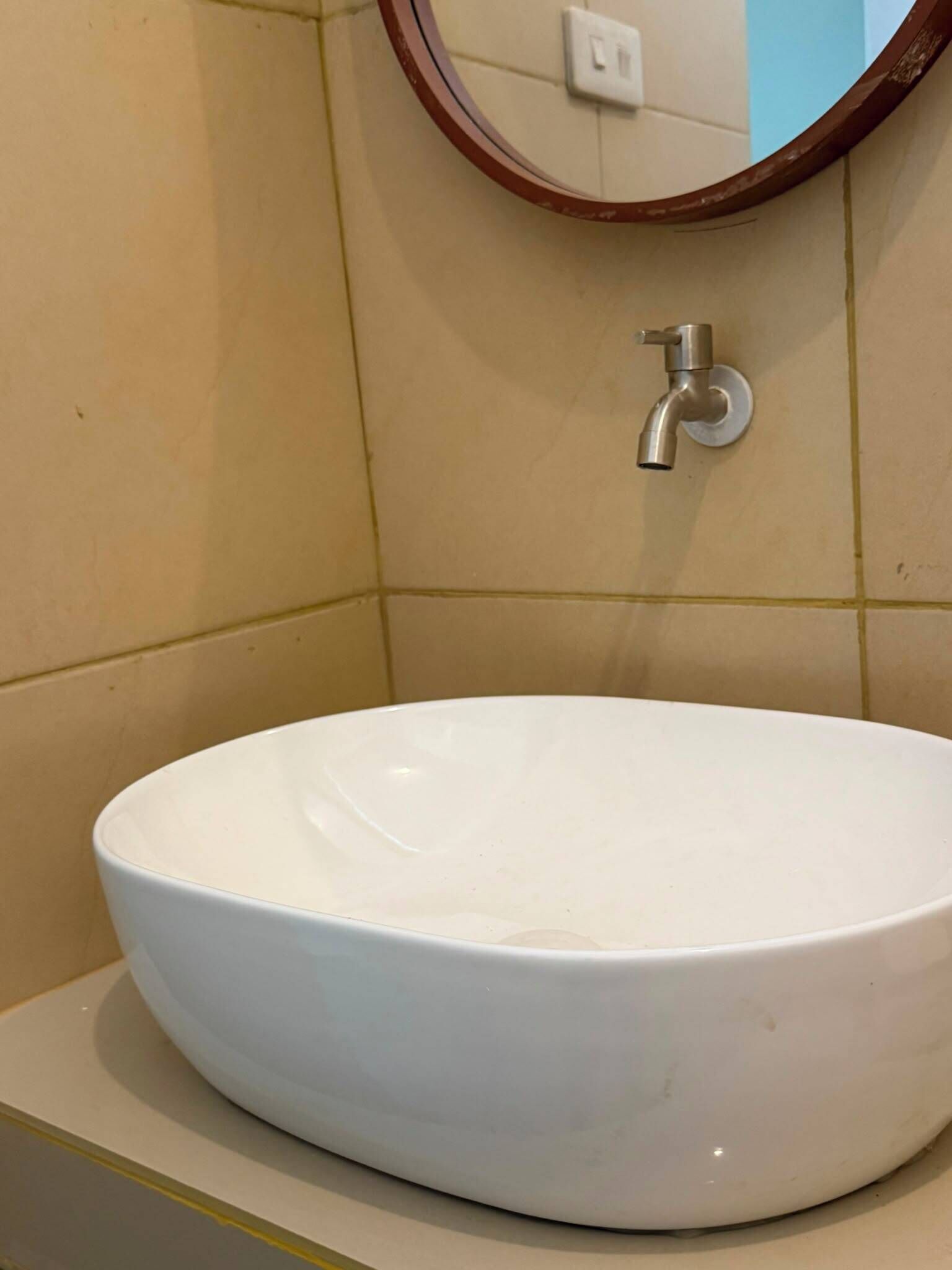A white ceramic sink with a round basin, mounted on a beige tiled wall with a single faucet.