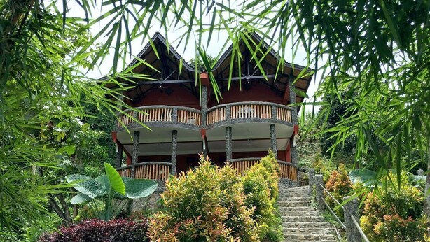 A multi-story building with a wooden balcony, surrounded by lush greenery and stone steps leading up to it. - Hotel Orangutan (Bukit Lawang)