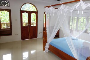 Un dormitorio con una cama con dosel, una puerta de madera y un ventanal con vistas a zonas verdes.