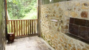 A stone-walled bathroom with a wooden bench, a shower area, and a view of greenery outside. - Hotel Orangutan (Bukit Lawang)