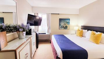 Quarto de hotel com cama, televisão de tela plana, escrivaninha com computador, espelho, janela com cortinas e um quadro na parede.