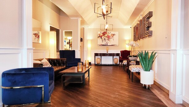 A spacious living room with a blue armchair, a sofa, and a coffee table. There is a fireplace with a mantel and a painting above it. - Western Lodge (Kimberley)