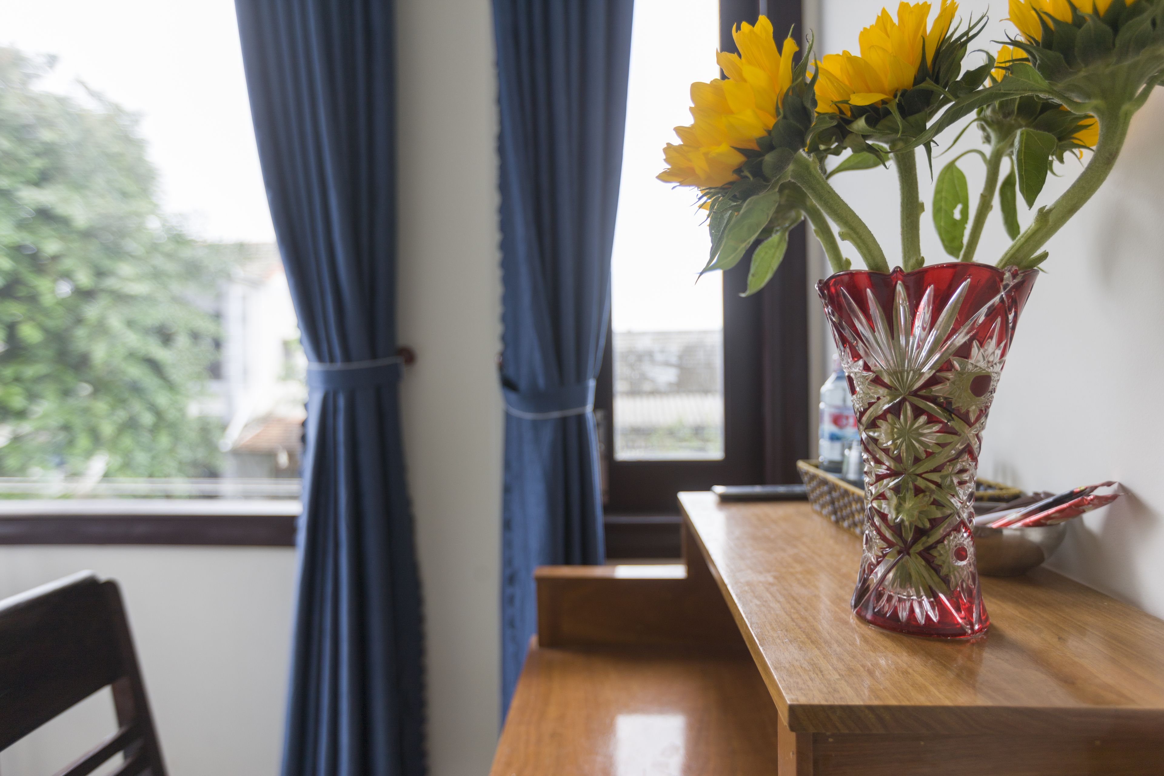 A wooden table with a red glass vase containing yellow flowers.