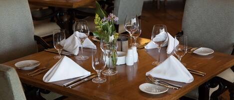 A dining table set with white napkins, silverware, and wine glasses, surrounded by upholstered chairs.