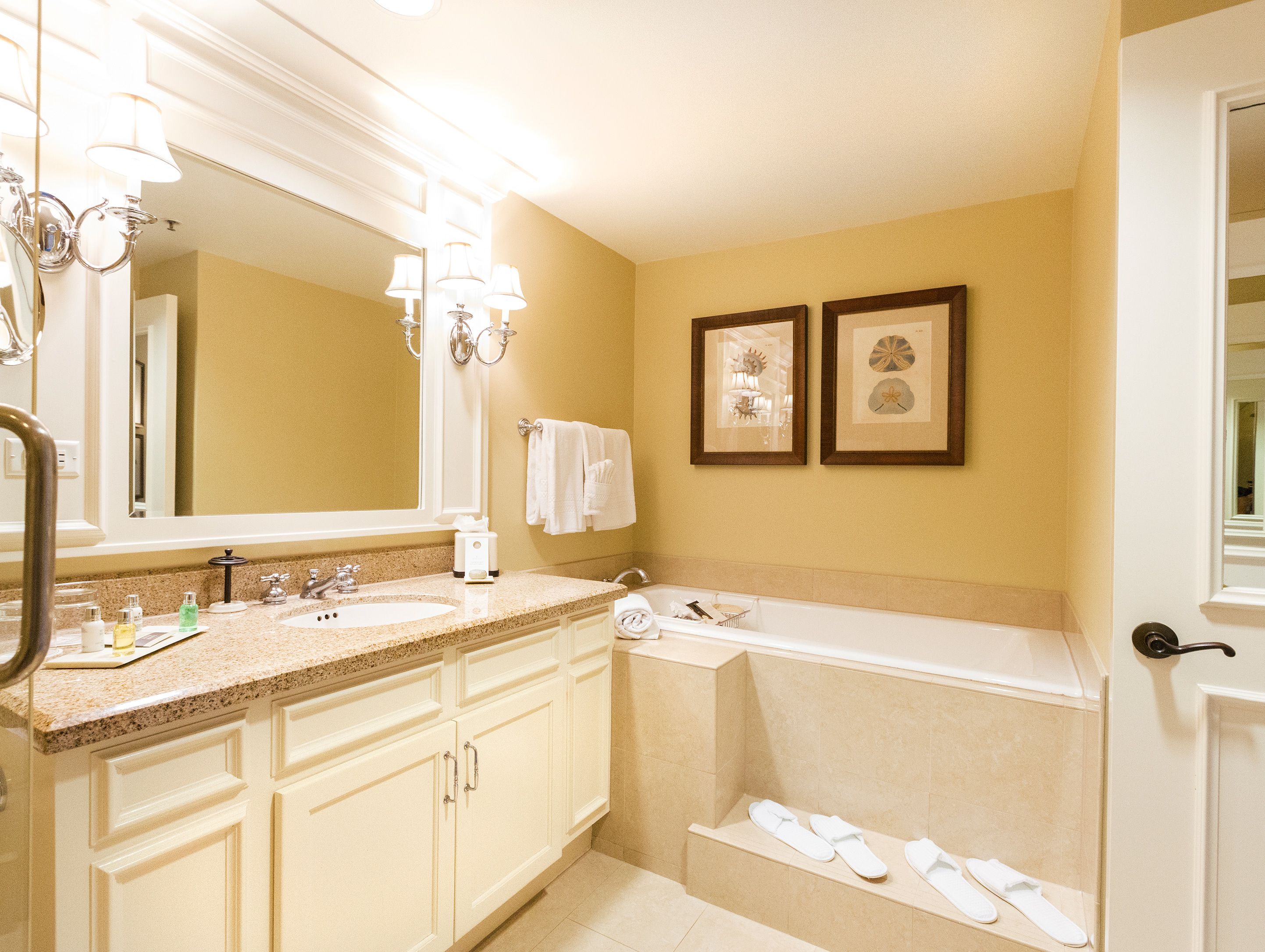 A bathroom with a double sink, a large mirror, a bathtub, and two framed pictures on the wall.