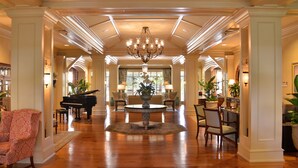 A spacious lobby with a grand chandelier, a piano, and a central floral arrangement. - The Inn & Club at Harbour Town (Hilton Head Island)