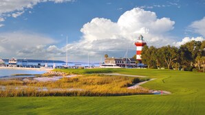 A golf course with a lighthouse, water, and boats in the background. - The Inn & Club at Harbour Town (Hilton Head Island)