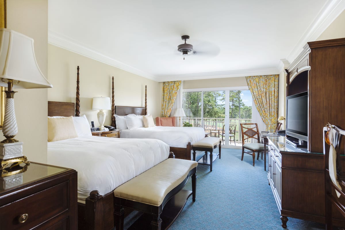 A hotel room with two beds, a desk, a chair, a TV, and a balcony with curtains.