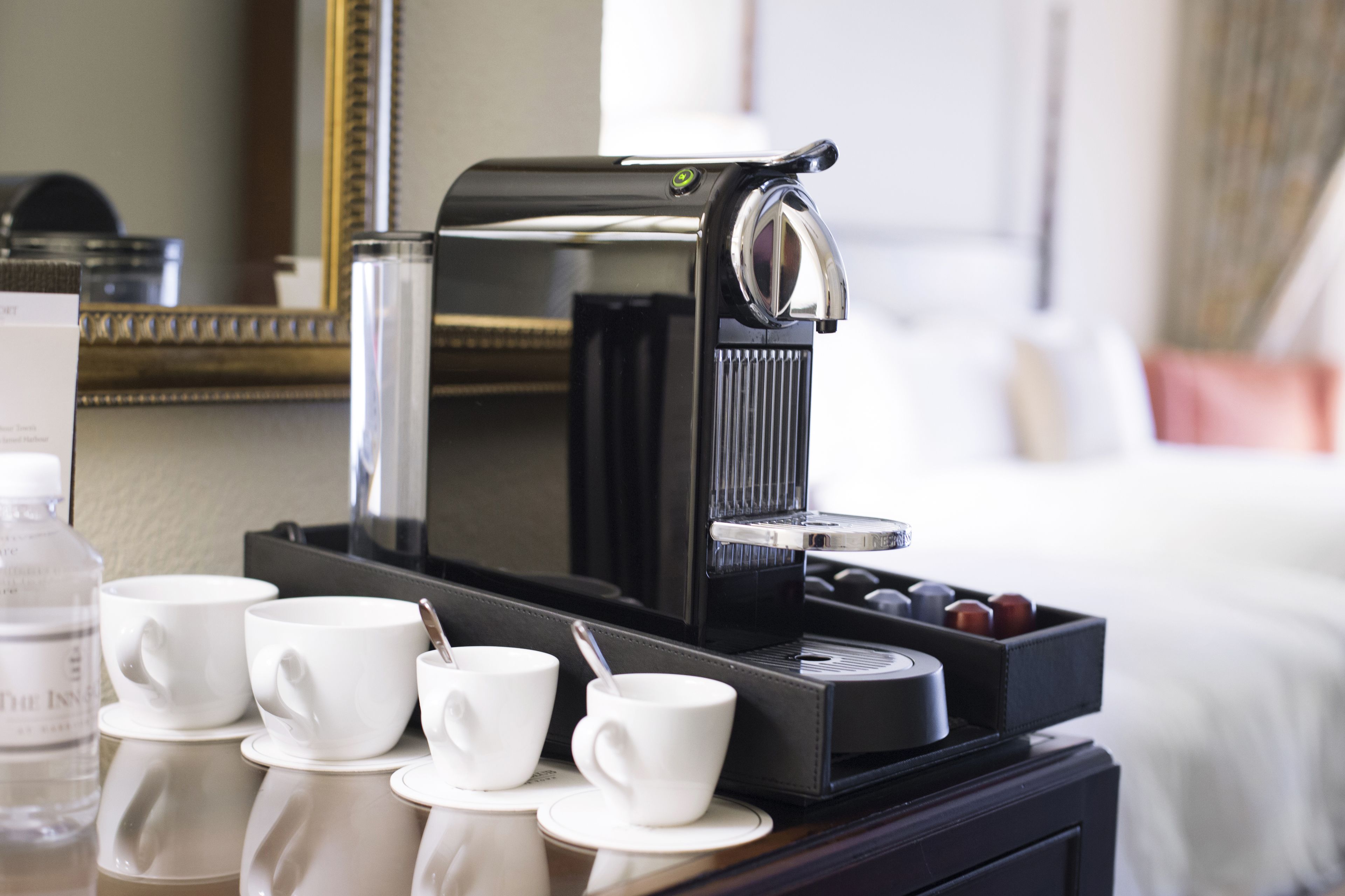 A coffee machine with four white cups and a water bottle on a table.