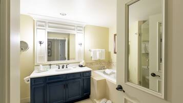 A bathroom with a double sink, dark blue cabinets, a large mirror, and a glass shower door.
