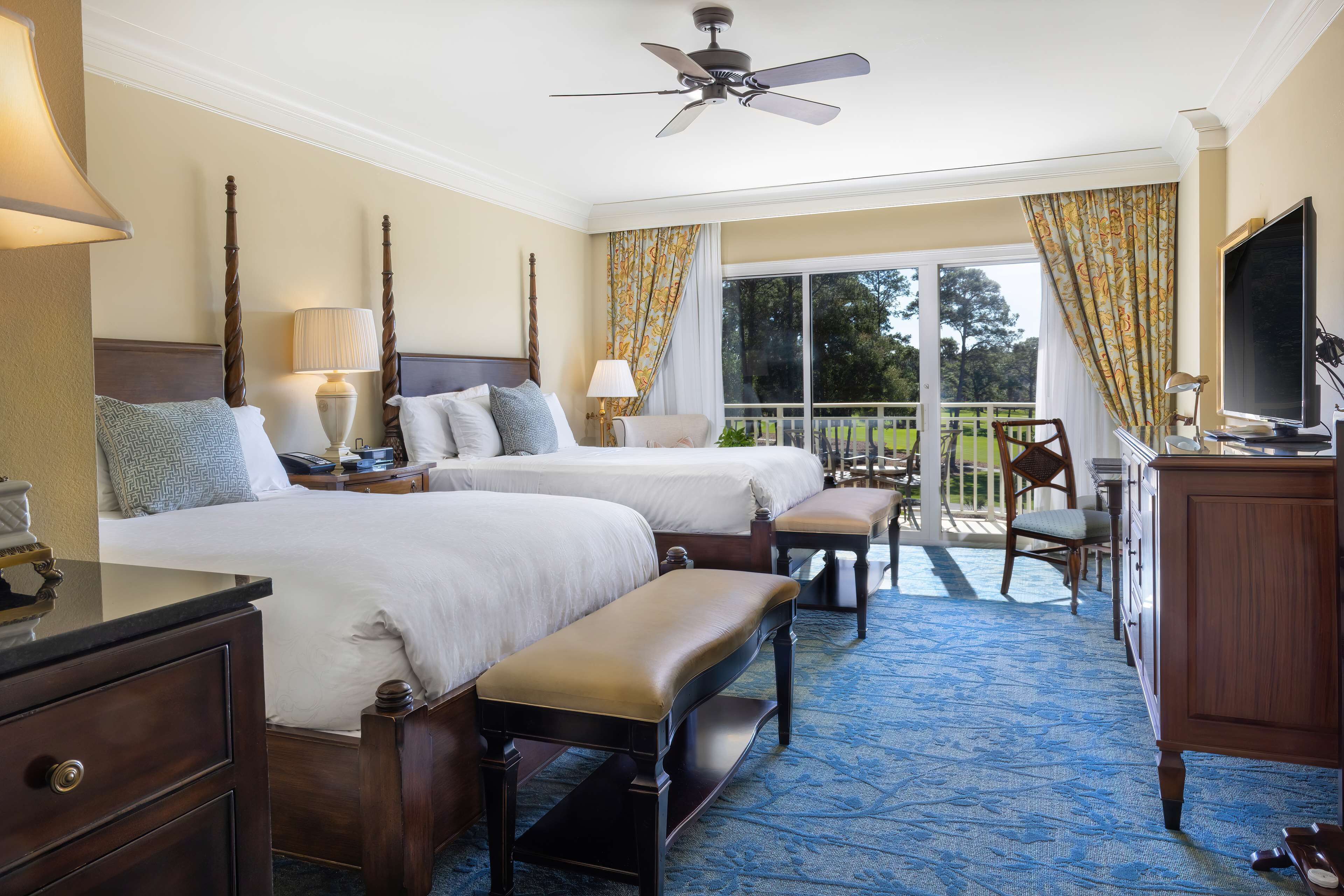 A hotel room with two beds, a desk, a chair, a television, and a balcony with a view of the outdoors.