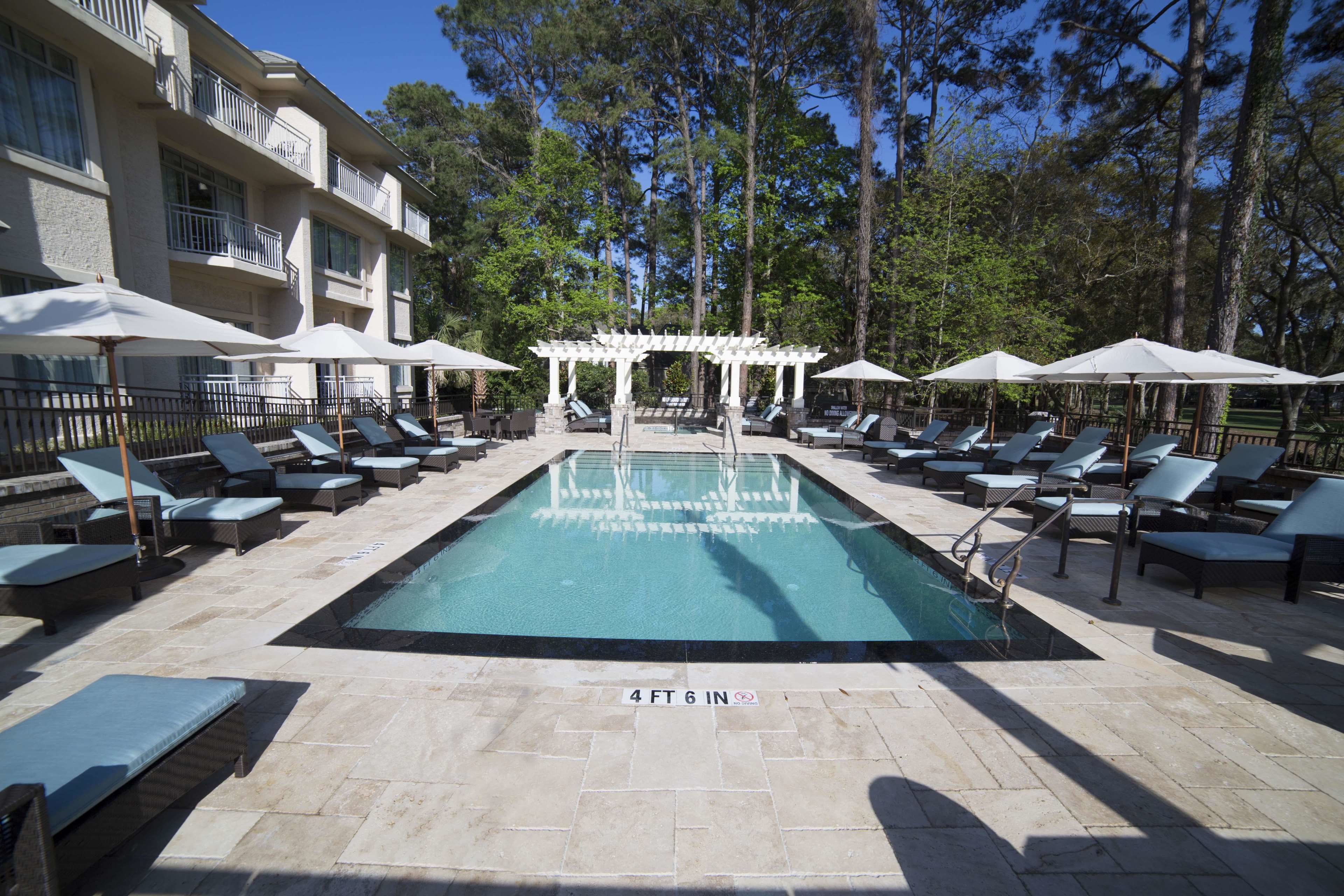 Un espace piscine agrémenté de chaises longues et de parasols, entouré d’arbres.