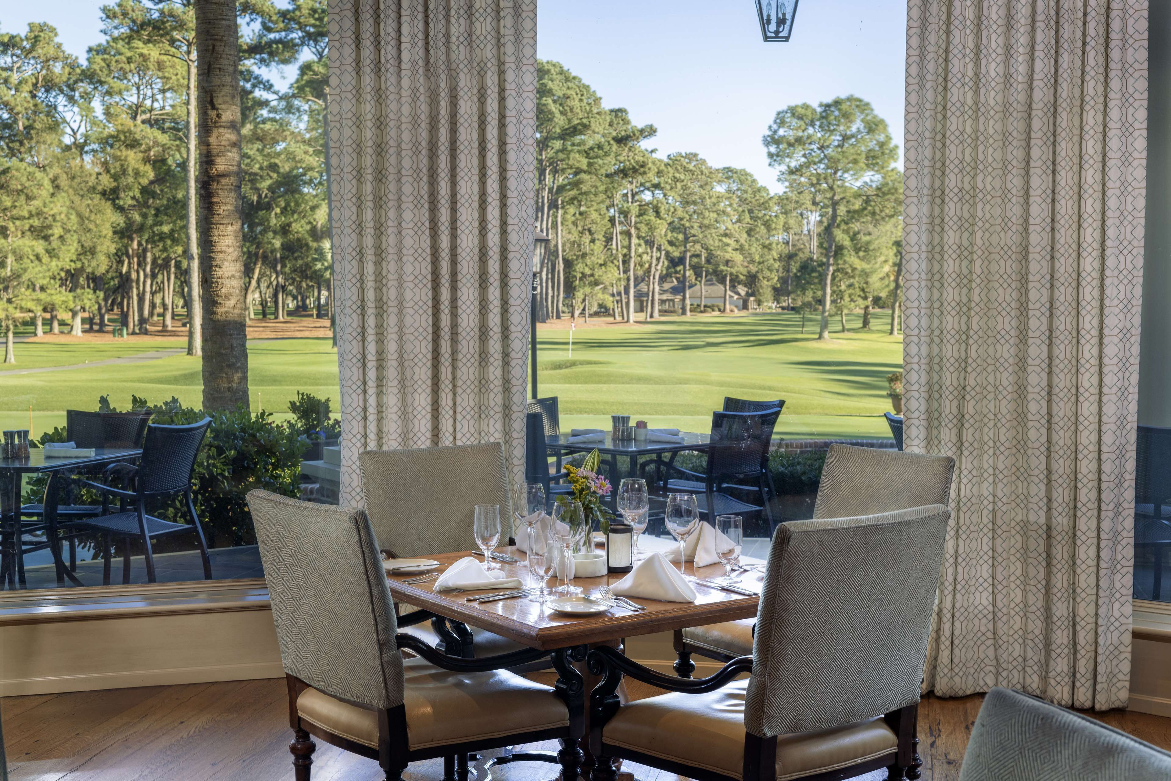 Tavolo da pranzo imbandito per due con vista su un campo da golf attraverso ampie finestre.