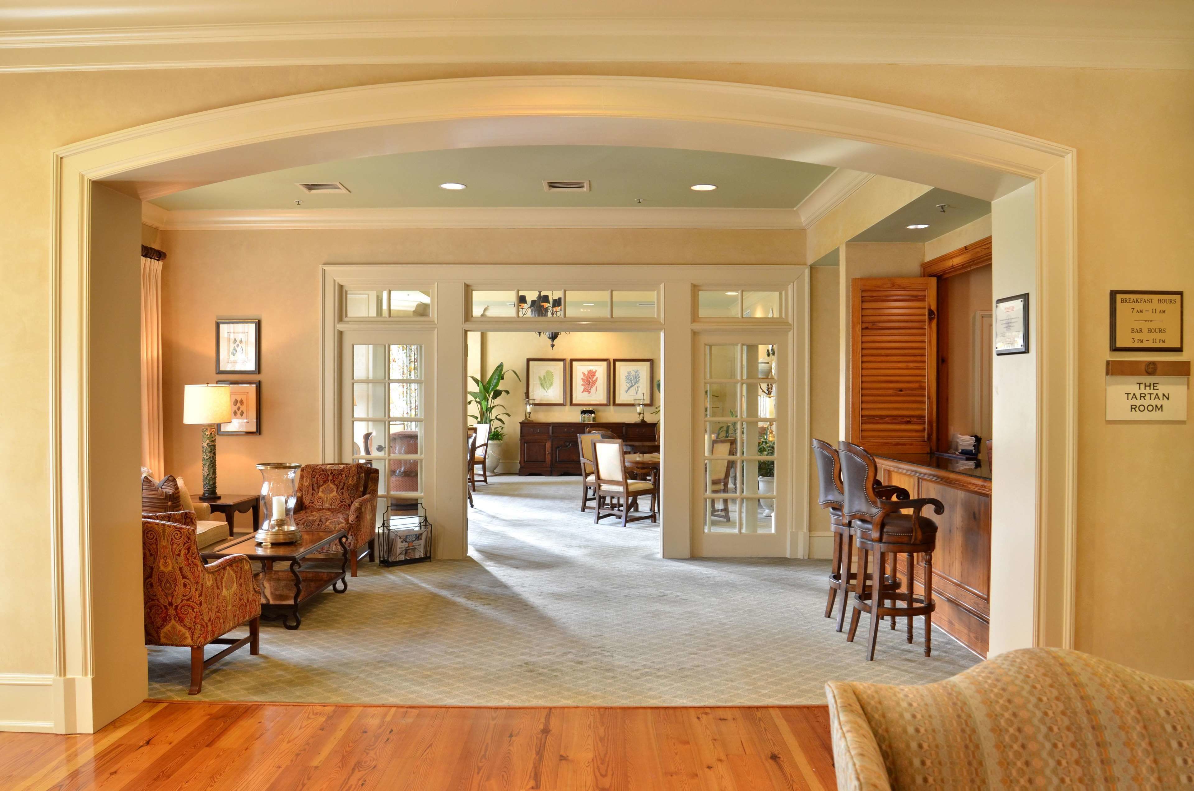A spacious living area with a wooden floor, a dining table, and comfortable seating. A kitchen area is visible in the background with a bar and stools.