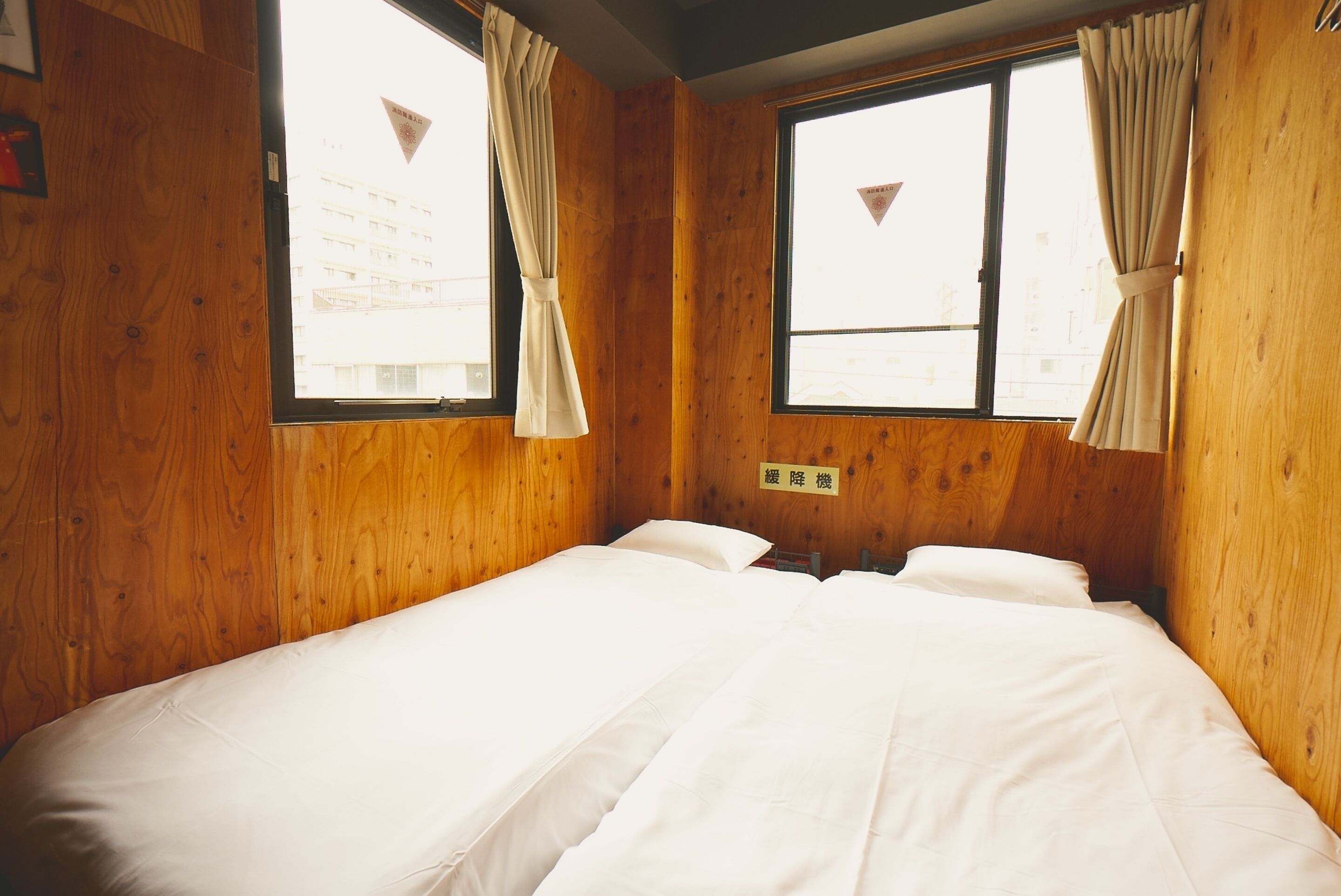 A wooden room with a bed, two windows with curtains, and a sign on the wall.