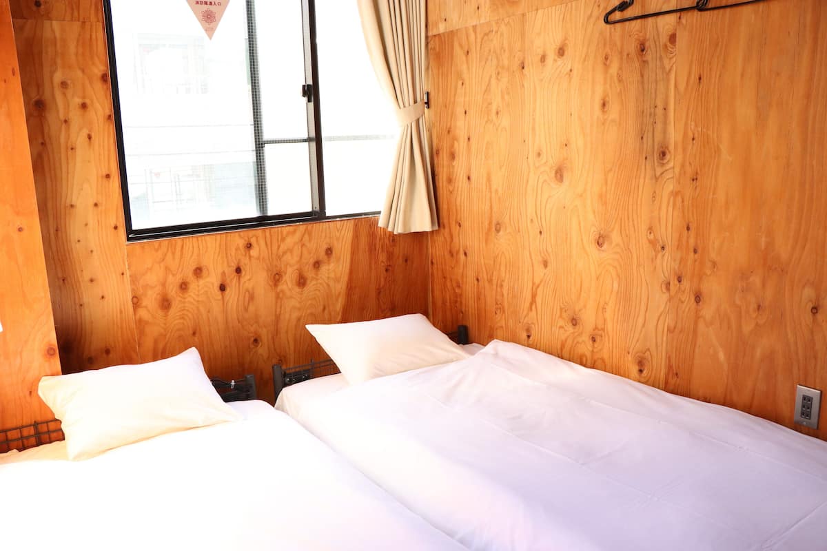Una habitación de madera con dos camas, una ventana con cortinas y un interruptor de luz en la pared.