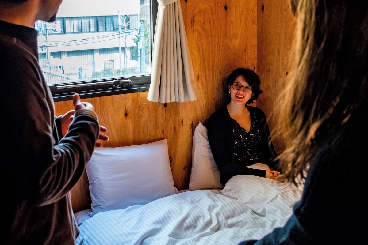 Una habitación con interior de madera, una cama con ropa de cama blanca y un ventanal con cortina.