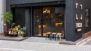A modern building with a black facade, a glass door entrance, and outdoor seating with tables and chairs. - FOCUS Kuramae - Hostel (Tokyo)