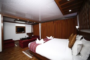A hotel room with a large bed, a red sofa, a TV mounted on the wall, and wooden paneling on the walls. - Hotel Sikkim Tourist Centre (Gyalshing)