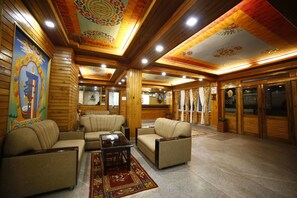 A traditional interior with wooden walls and ceilings, a central seating area with sofas and a coffee table, and decorative wall art. - Hotel Sikkim Tourist Centre (Gyalshing)