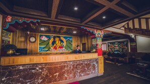 A reception desk with a wooden finish and a marble base, flanked by colorful murals and traditional decor. - Buddha Retreat (Namchi)