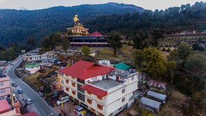 A large golden statue atop a temple, surrounded by a town with buildings and a road. - Buddha Retreat (Namchi)