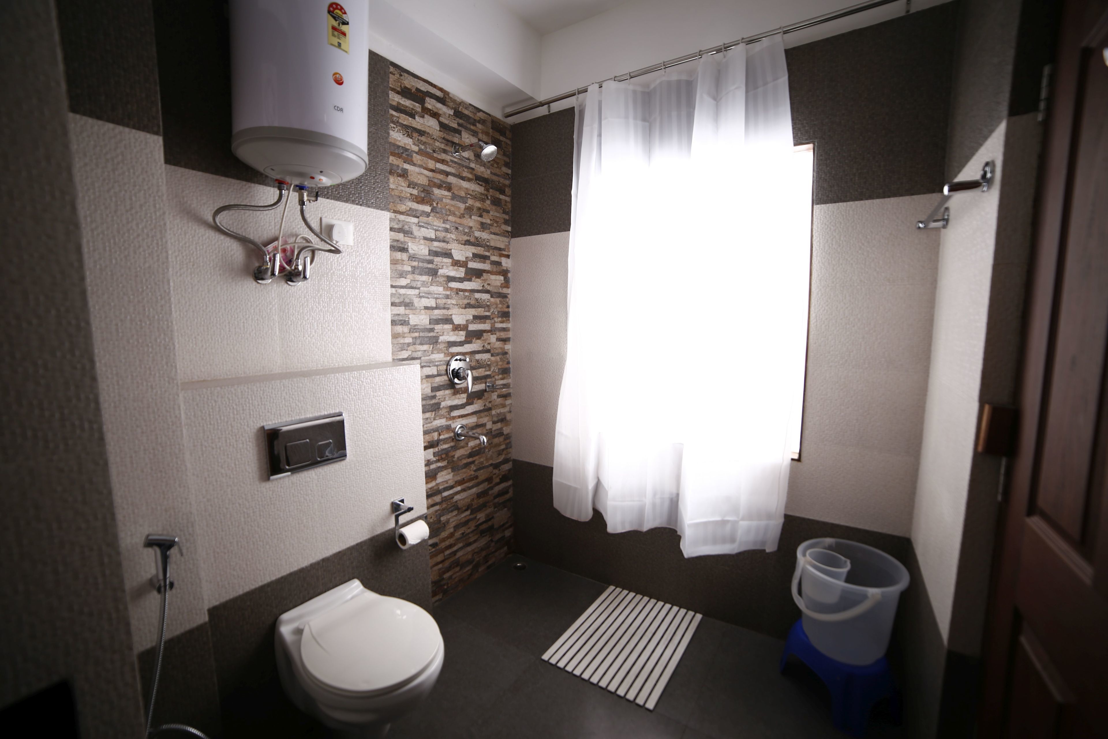 A modern bathroom with a toilet, shower, and a water heater mounted on the wall.