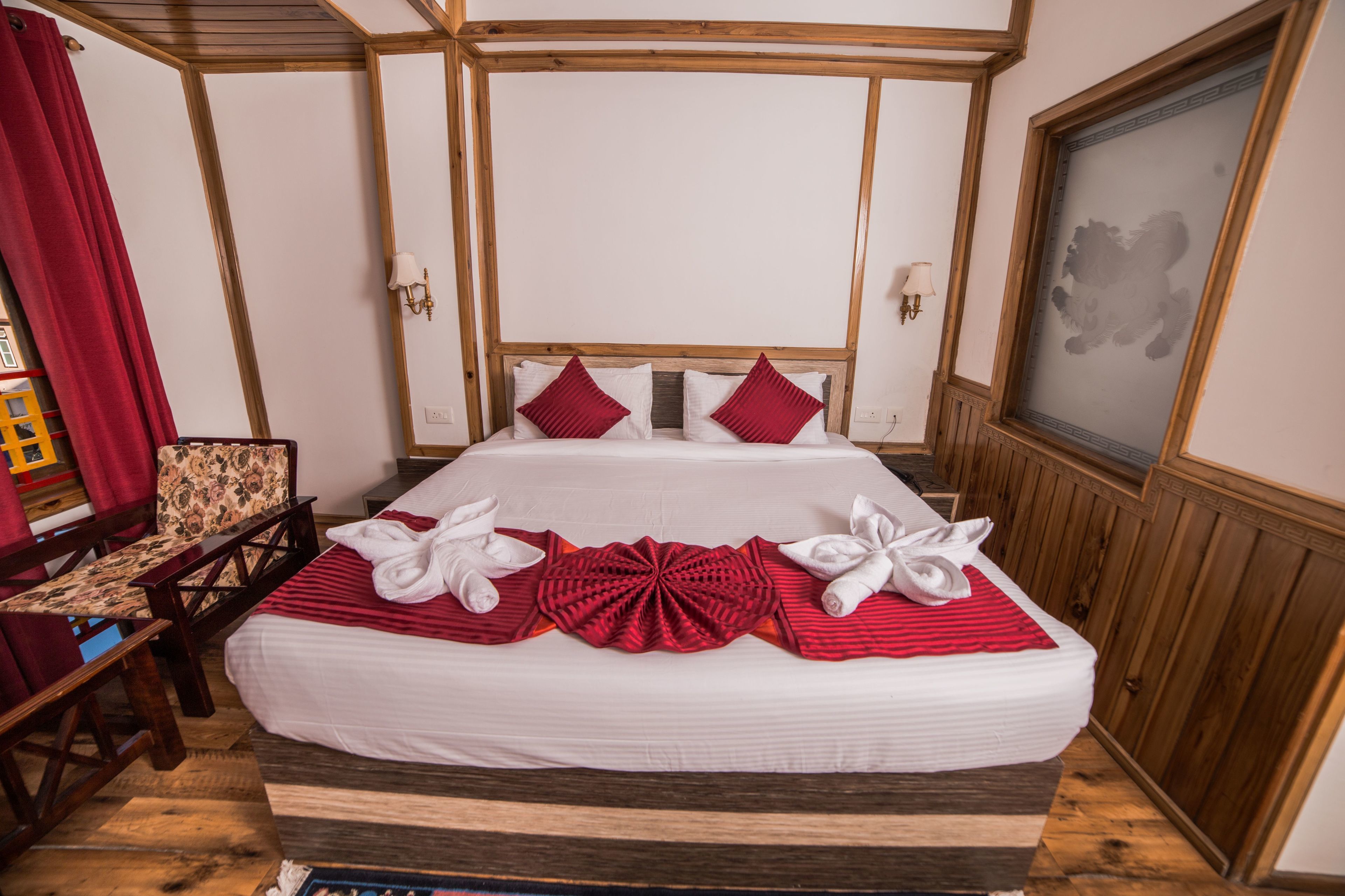 A neatly made bed with white and red linens, a wooden headboard, and a red throw blanket.