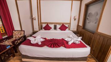 A neatly made bed with white and red linens, a wooden headboard, and a red throw blanket.