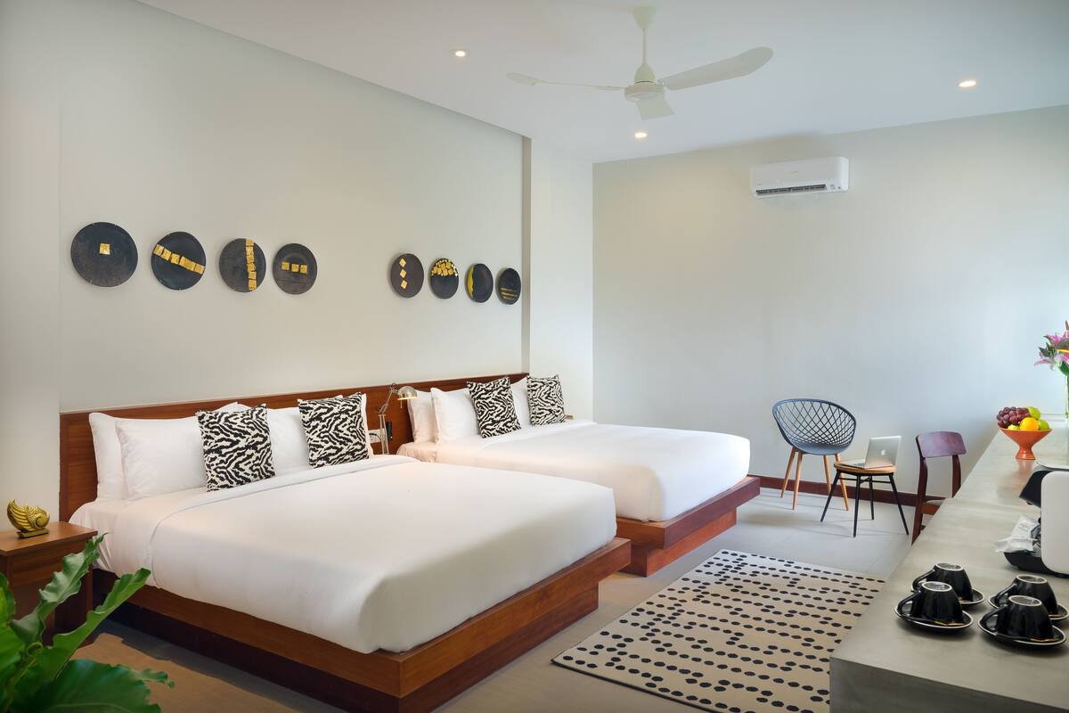 A hotel room with two beds, a desk, a chair, a coffee machine, and a wall with decorative plates.