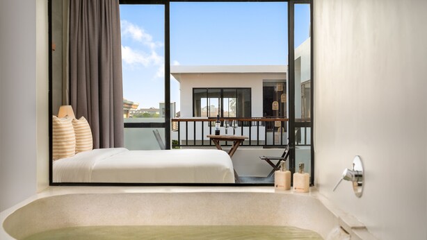 A modern hotel room with a large bathtub, a balcony with a table and two wine glasses, and a view of the cityscape. - Gold Smith Residence (Siem Reap)