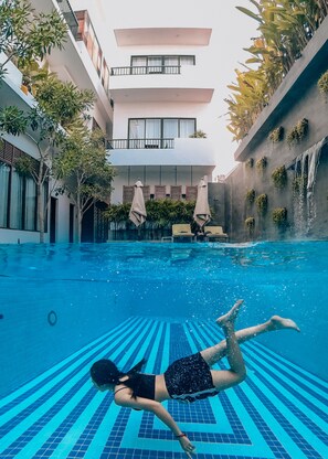 An indoor swimming pool with clear blue water, a tiled floor, and a person swimming. - Gold Smith Residence (Siem Reap)