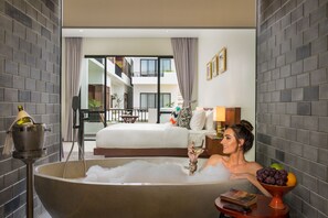 A modern hotel room with a large bathtub, a dining area with a balcony, and a view of the building's interior. - Gold Smith Residence (Siem Reap)