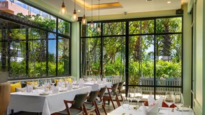A restaurant with tables set for dining, large windows with a view of greenery, and hanging pendant lights. - Gold Smith Residence (Siem Reap)