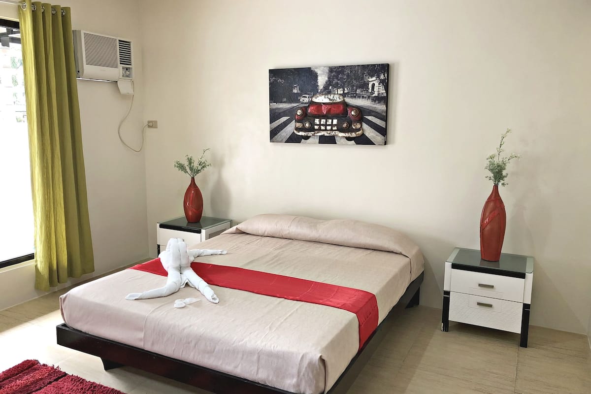 Una habitación de hotel con una cama, una mesita de noche, un jarrón y un cuadro en la pared.