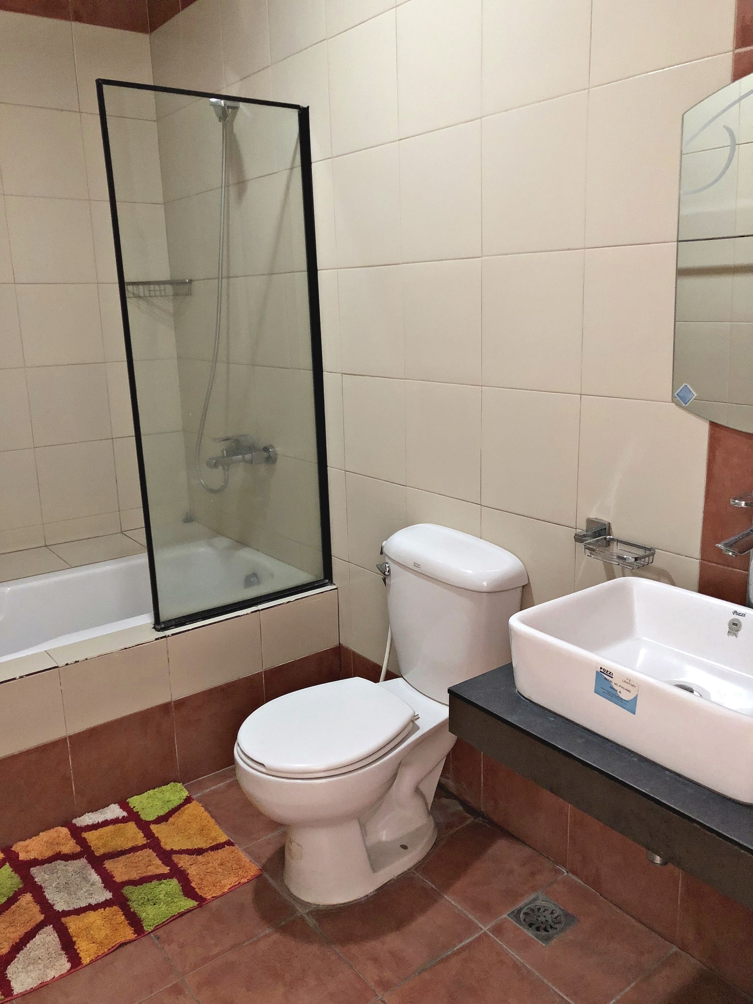 Un baño con ducha envuelta en vidrio, un inodoro blanco y un lavamanos con espejo.