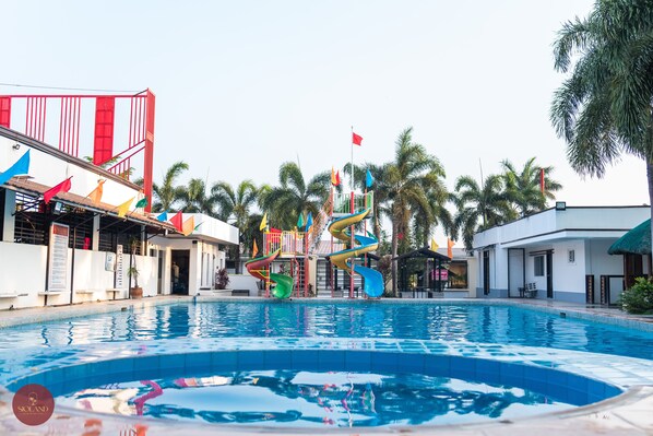 A swimming pool with colorful slides and palm trees in the background.