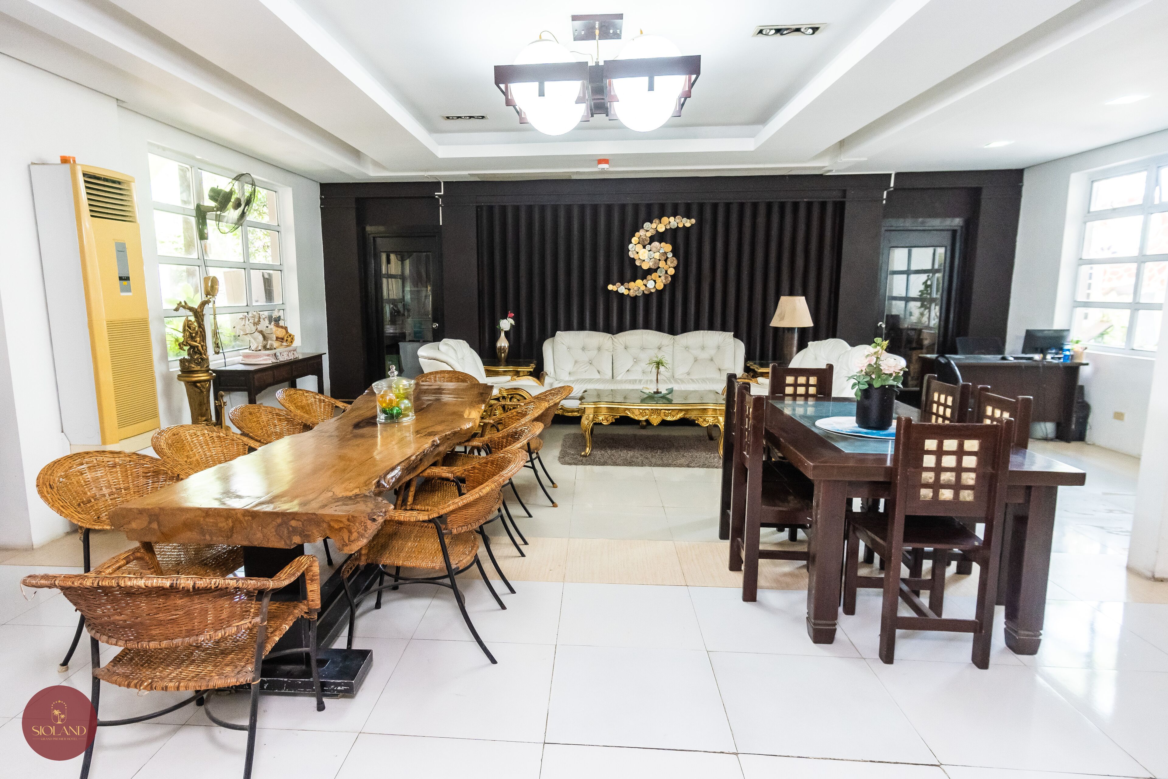 A spacious dining area with a long wooden table and wicker chairs, a white sofa, and a decorative wall piece.