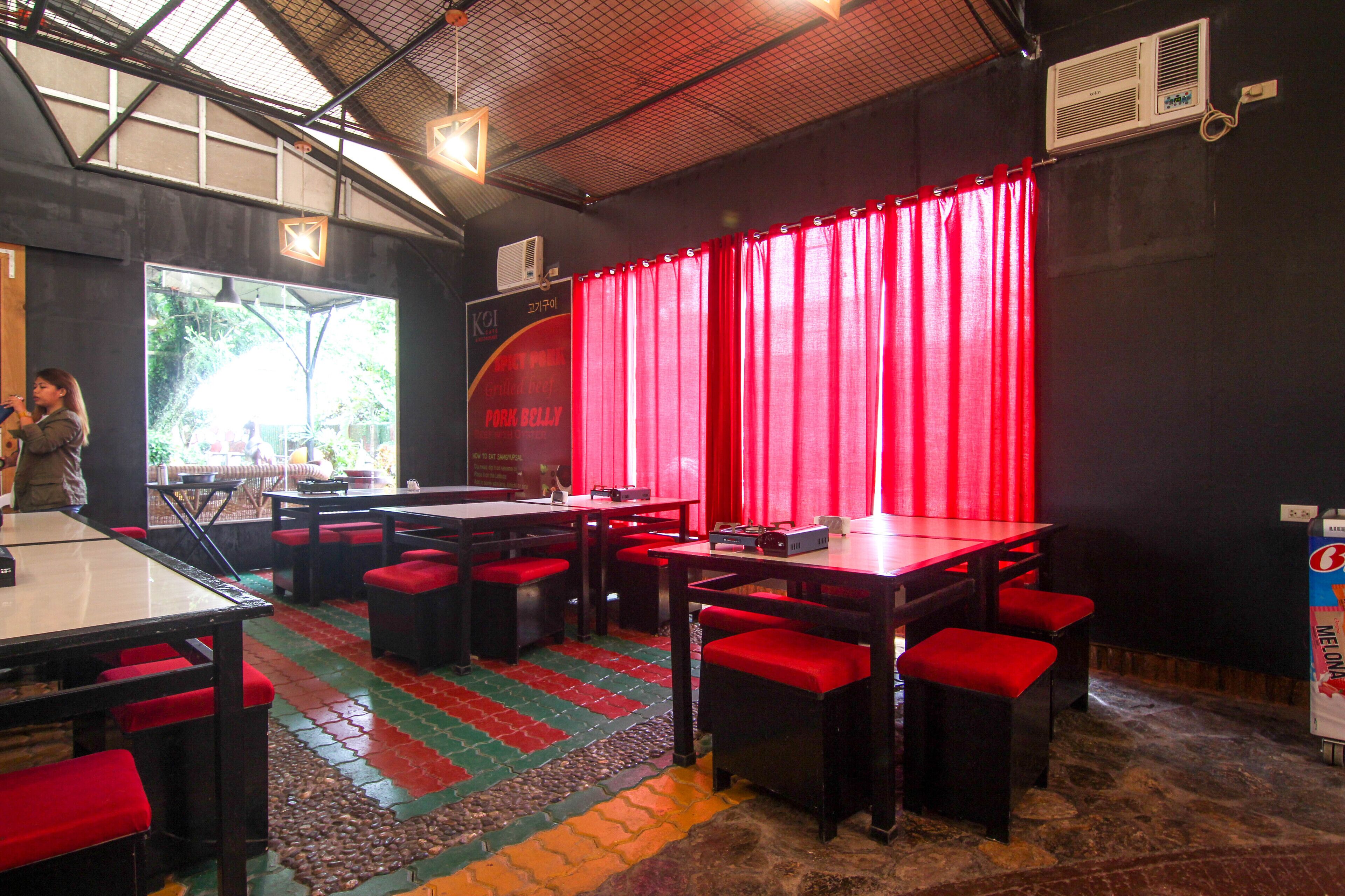 Un restaurante con cortinas rojas, varias mesas y asientos acolchados en rojo.