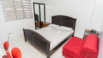 A bedroom with a bed, a red sofa, a wooden wardrobe, and a mirror.