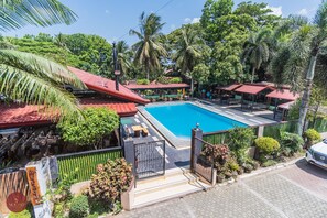 A swimming pool surrounded by a fenced area with outdoor seating and a red-roofed building. - Quezon Premier Hotel Lucena (Lucena)