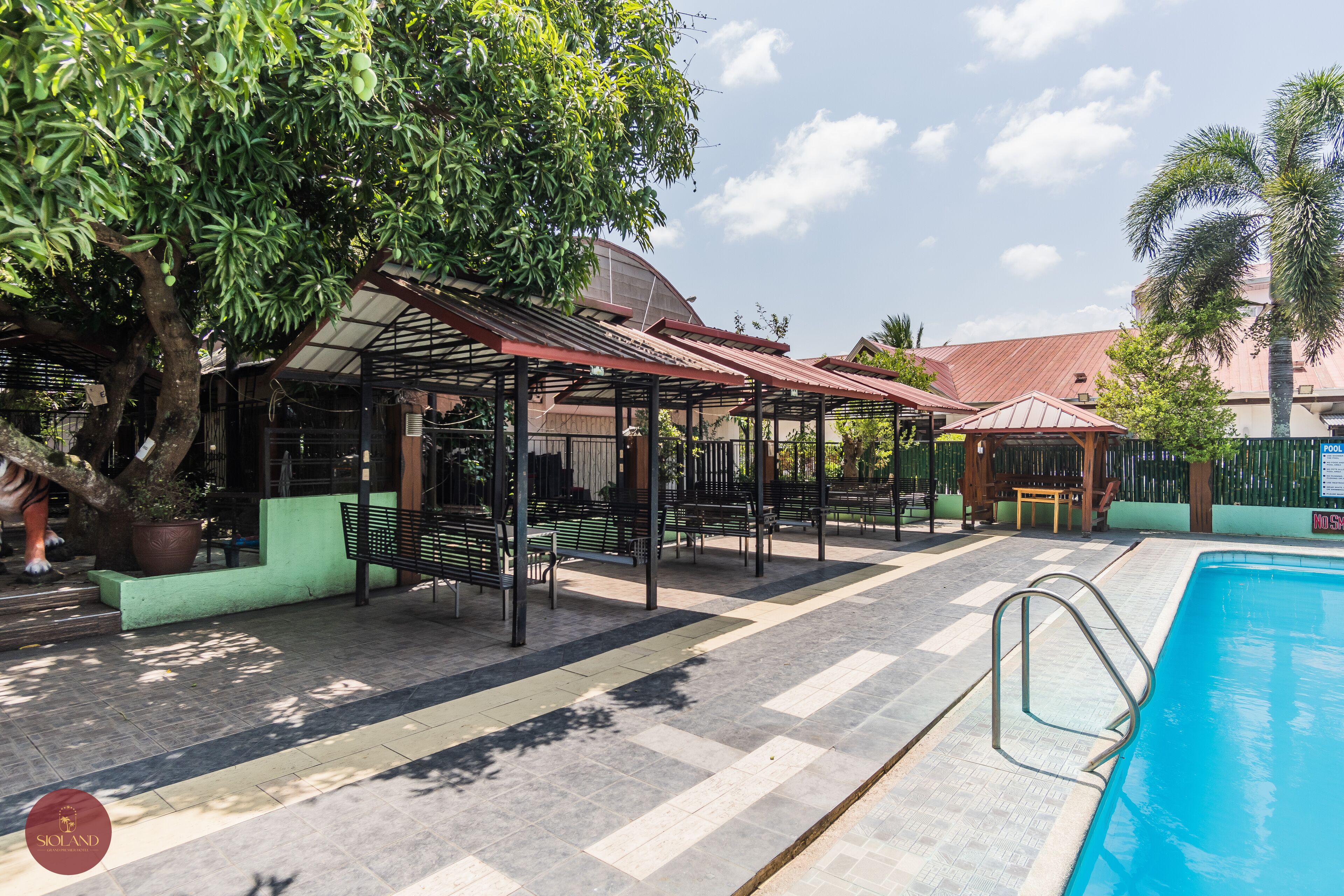 A poolside area with a covered seating area, a pool, and a building in the background.