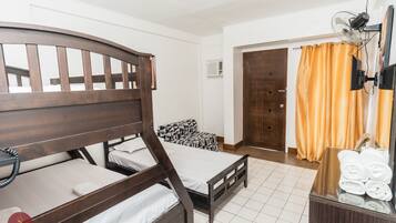 Ein Hotelzimmer mit zwei Holzbett, einem kleinen Sofa, einem Spiegel, einem Ventilator und einer Holzkombination mit Handtüchern.