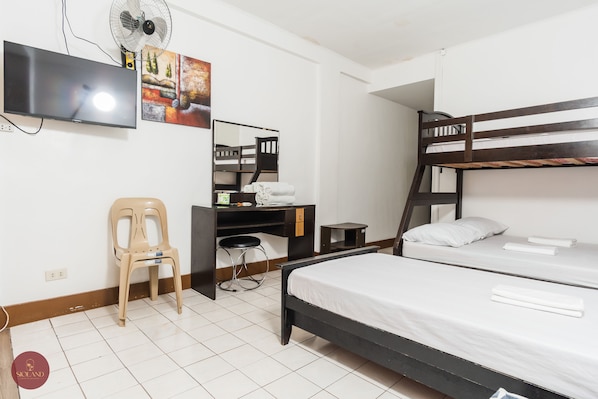 Un dormitorio con literas, un escritorio con silla, un televisor y un ventilador.
