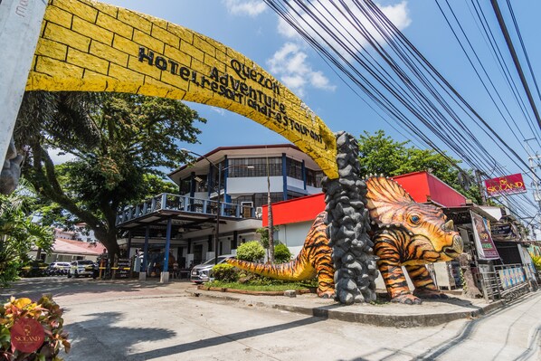 A hotel entrance with a large tiger statue, a yellow sign, and a building with balconies.