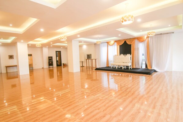 A spacious room with a polished wooden floor, a stage with a white chair, and a large window with curtains. - Quezon Premier Hotel Lucena (Lucena)